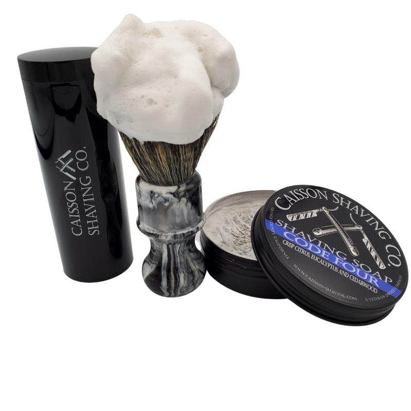 Caisson Code Four shaving soap with a lathered synthetic brush and travel container.