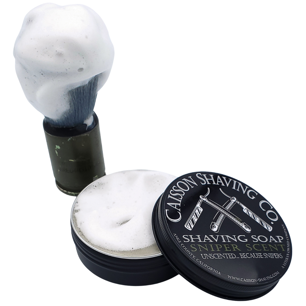 Lathered shaving brush beside an open can of Sniper Scent shaving soap.