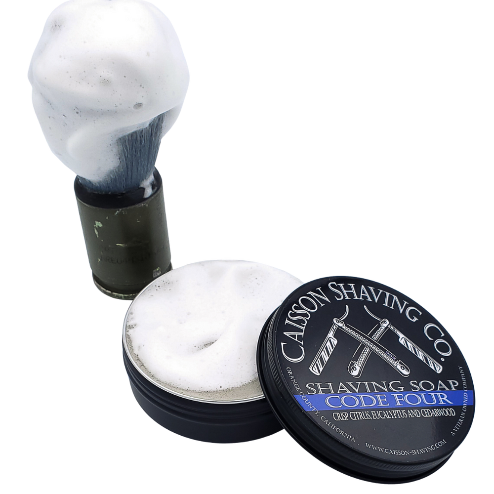 Lathered shaving brush beside an open can of Code Four shaving soap.